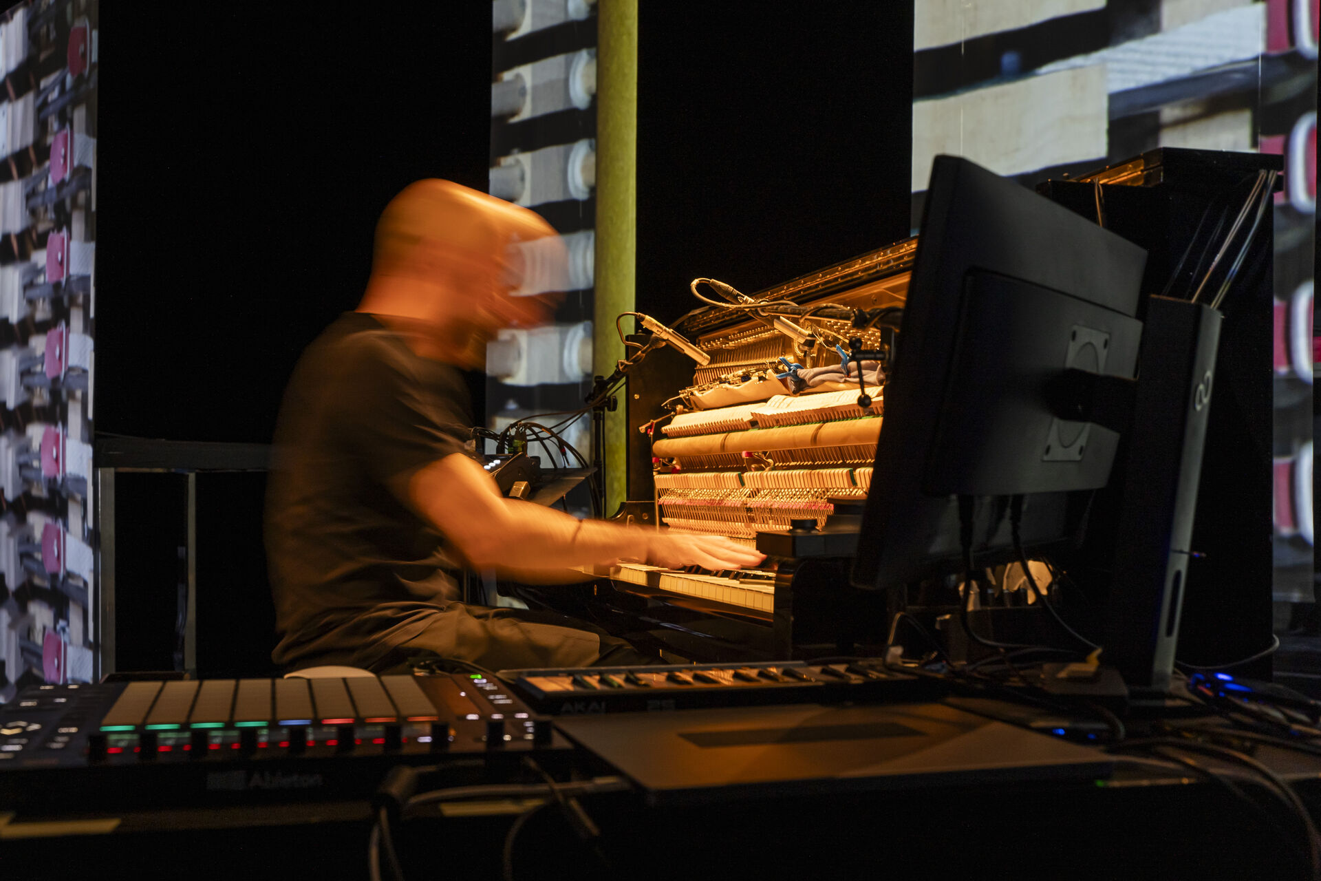 Expanded Piano II: Gasparatos in motion blur as he plays an open piano with exposed strings; an Akai controller and laptop are visible in the foreground. Photo by Andreas Simopoulos.
